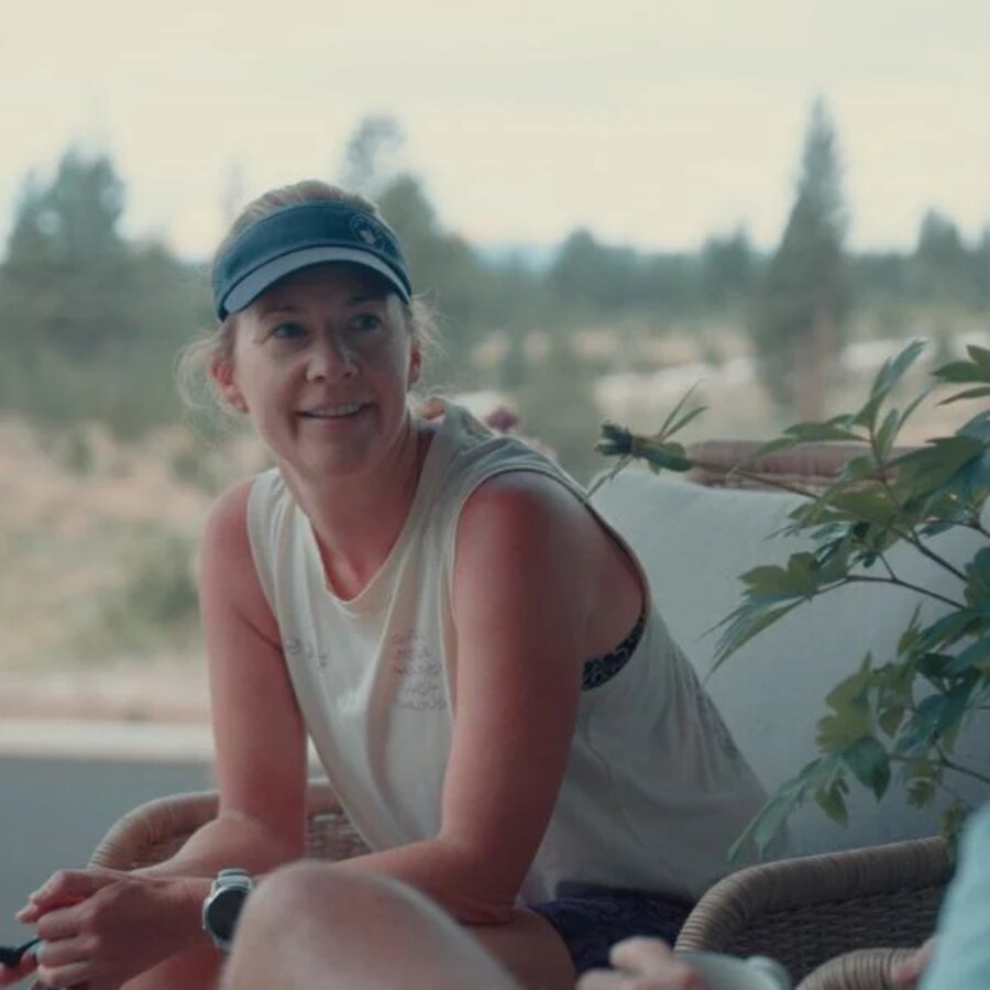 Joella Nicole seated outdoors in running attire beside leafy greenery